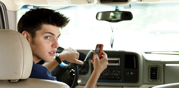 Teen boy with cell phone behind the wheel